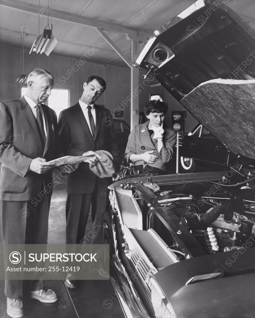 Stock Photo: 255-12419 Senior man showing a car to a mid adult couple in a showroom