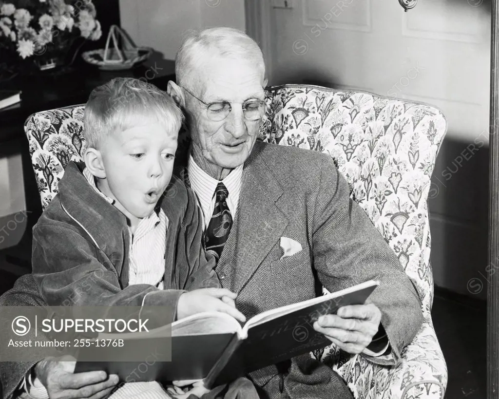 Close-up of a boy sitting on his grandfather's lap and reading a book