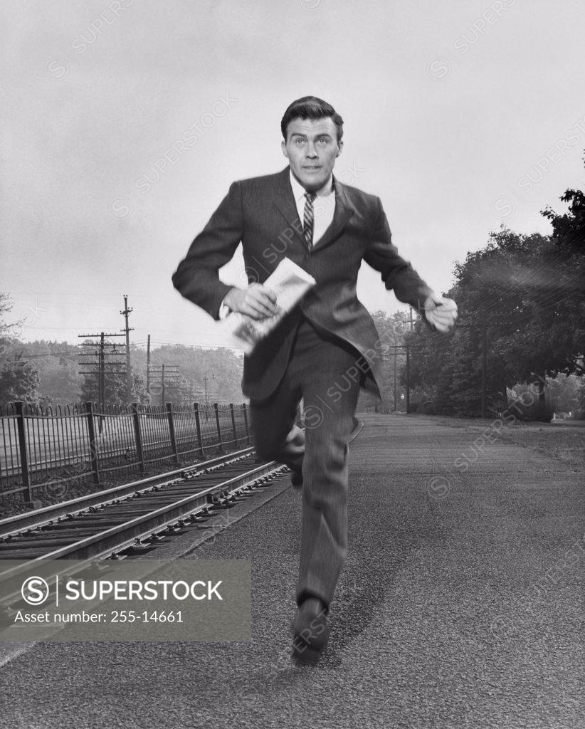 Stock Photo: 255-14661 Businessman running along a railroad track carrying a newspaper