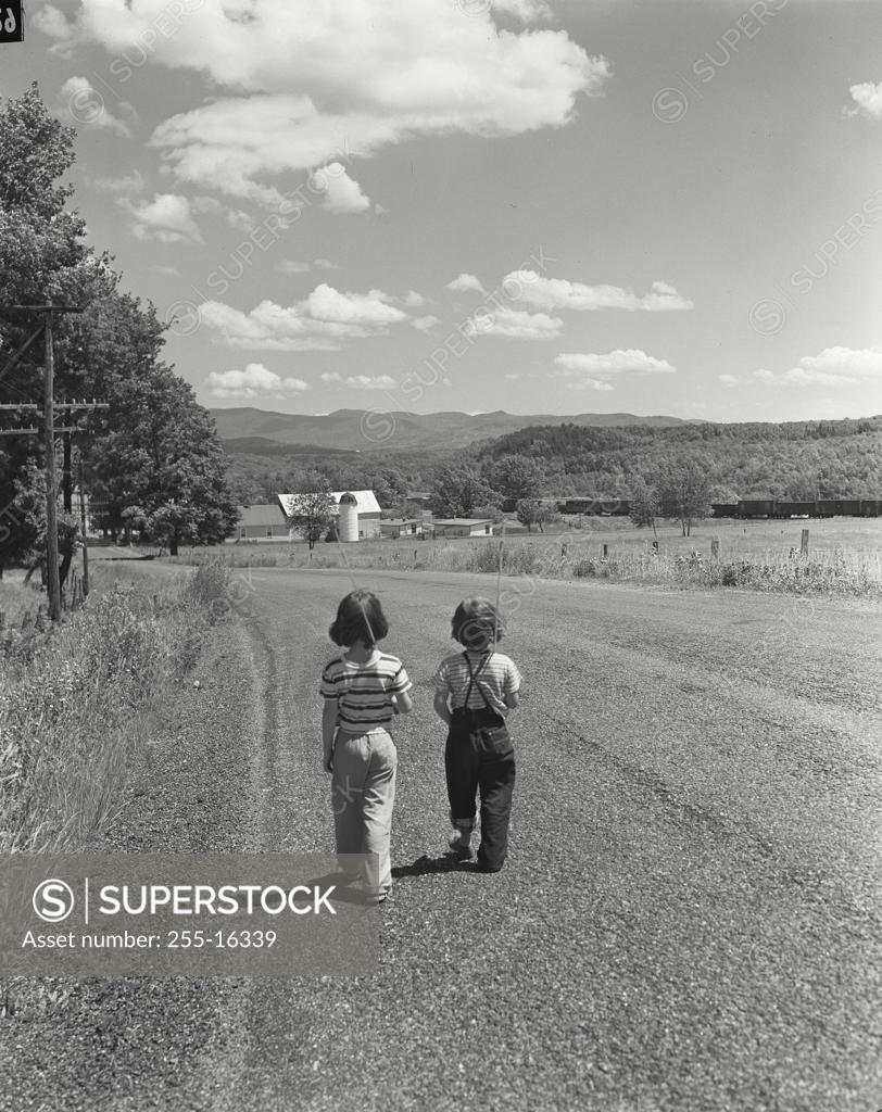 Stock Photo: 255-16339 Rear view of two girls walking together on a road