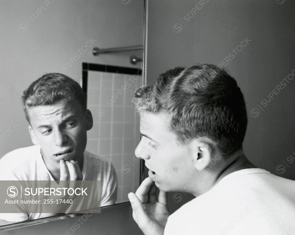 Stock Photo: 255-17440 Rear view of a teenage boy looking at a mirror with his hand on his chin, 1960