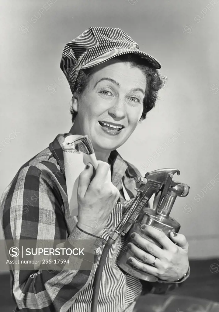 Middle aged woman smiling and dressed in work uniform holding paint sprayer and envelope of money