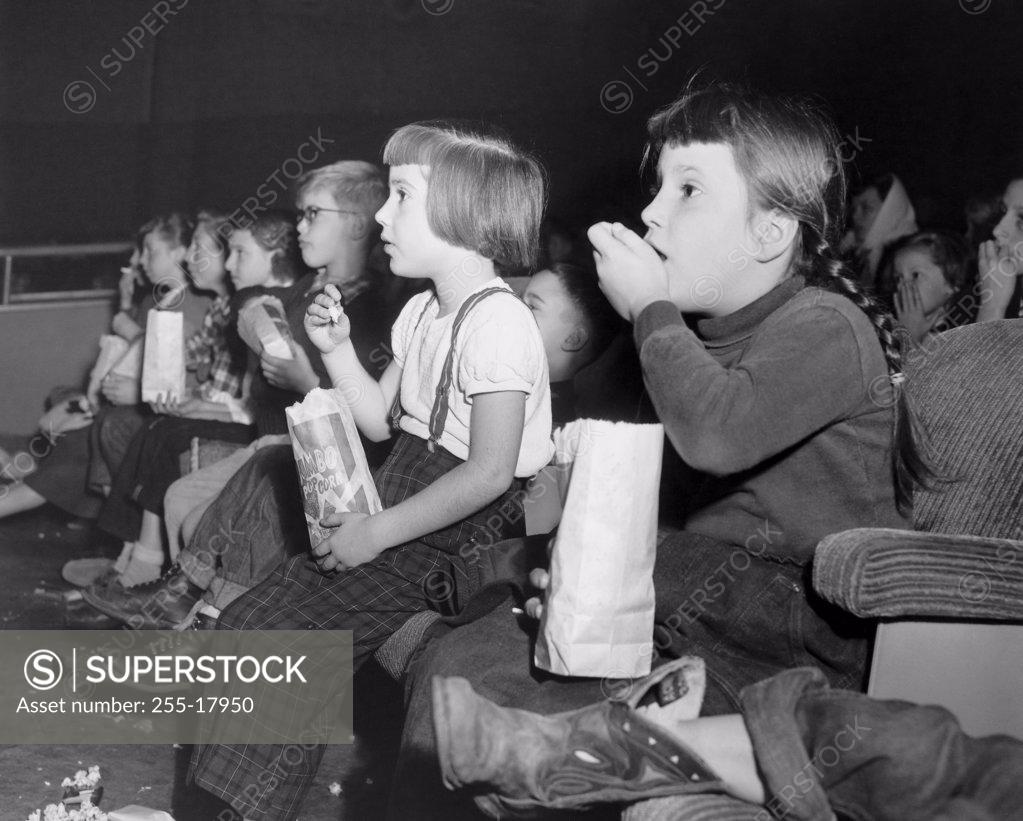 Stock Photo: 255-17950 Side profile of a group of children eating popcorn while watching a movie in a movie theater