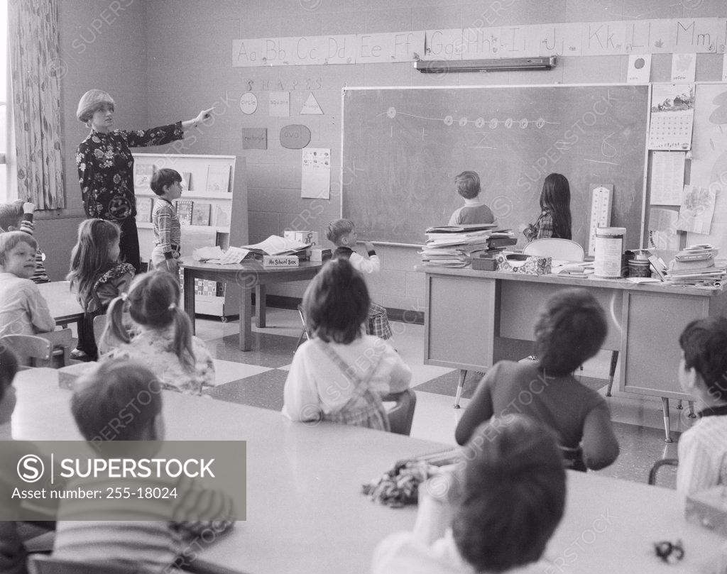 Stock Photo: 255-18024 Female teacher pointing to a blackboard