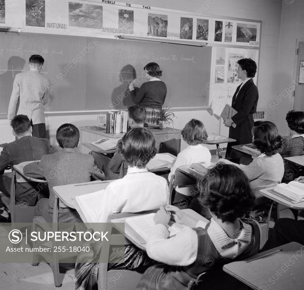 Stock Photo: 255-18040 Rear view of a boy and a girl writing on a blackboard in a classroom