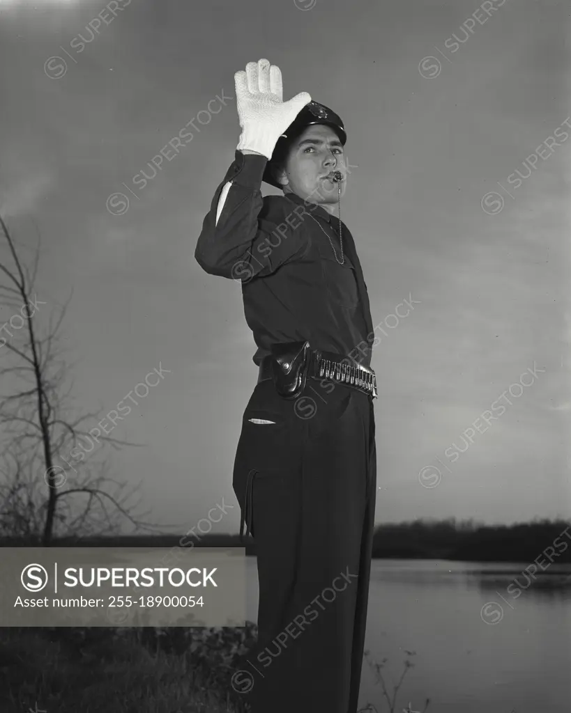 Vintage photograph. Policeman blowing whistle while holding up hand