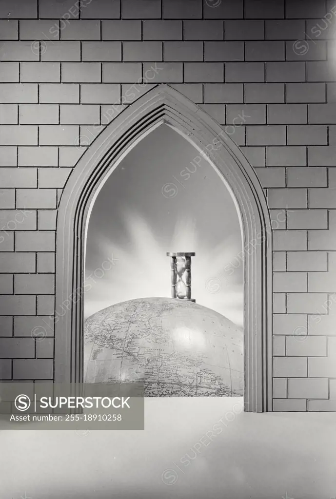 Vintage photograph. Photo illustration of pointed brick arch looking through to sand timer sitting on globe of the world