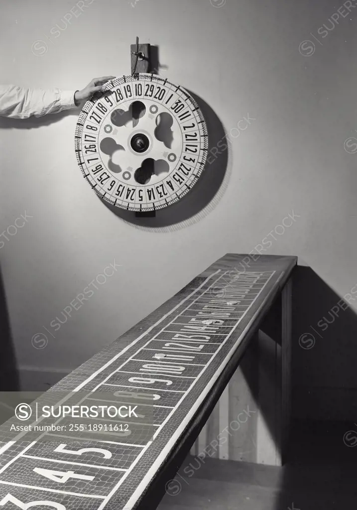 Vintage photograph. Hand about to spin Carnival Wheel on wall with betting board in foreground