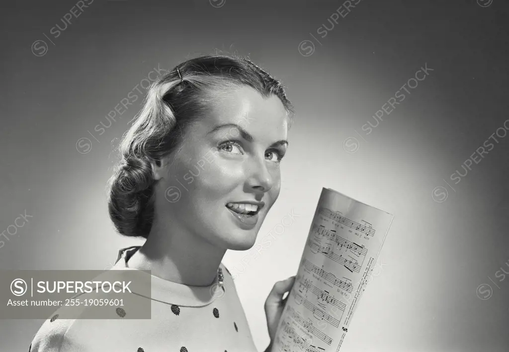 Vintage photograph. Woman with short hair in polka dot blouse holding sheet music.