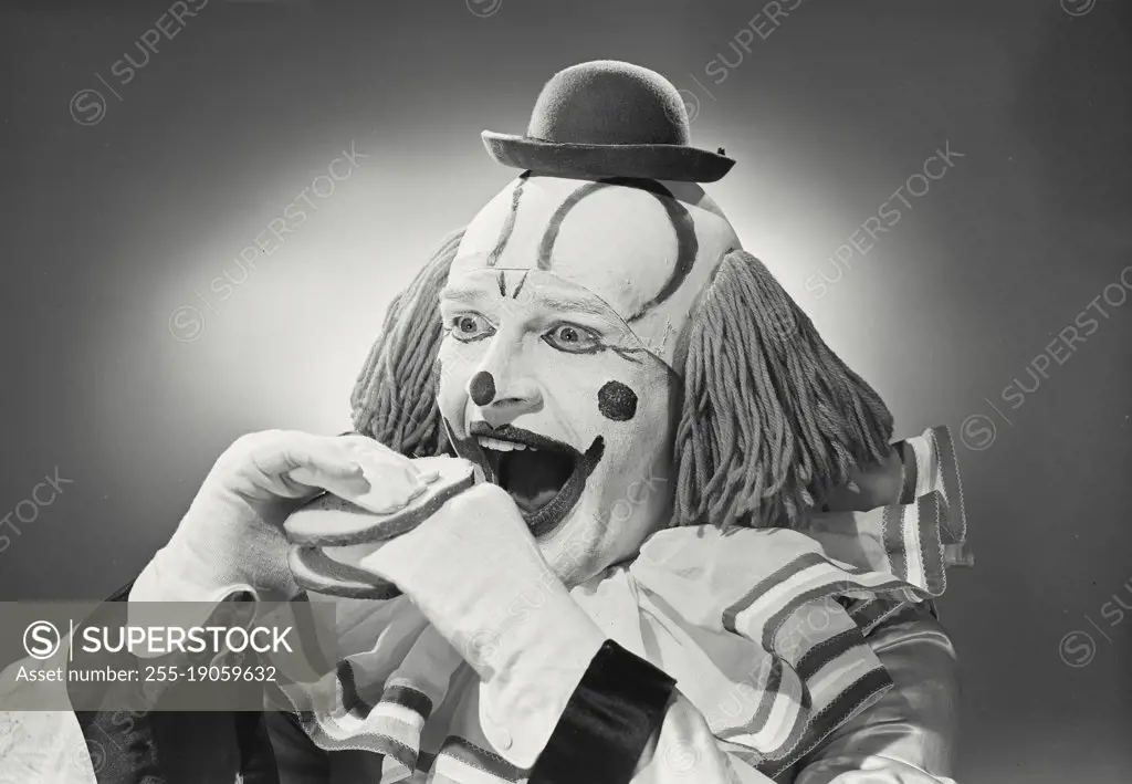 Vintage photograph. Portrait of clown wearing silly hat with hand sandwiched between two pieces of bread.