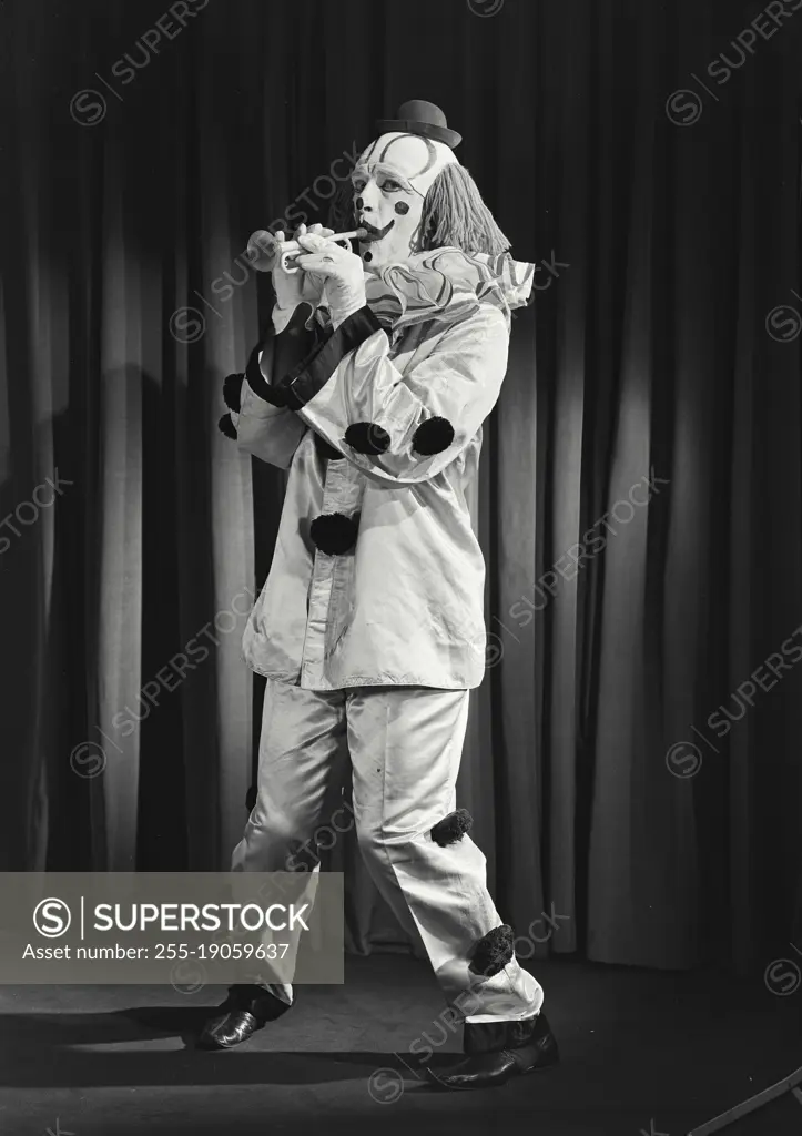 Vintage photograph. Portrait of clown wearing silly hat and playing toy horn