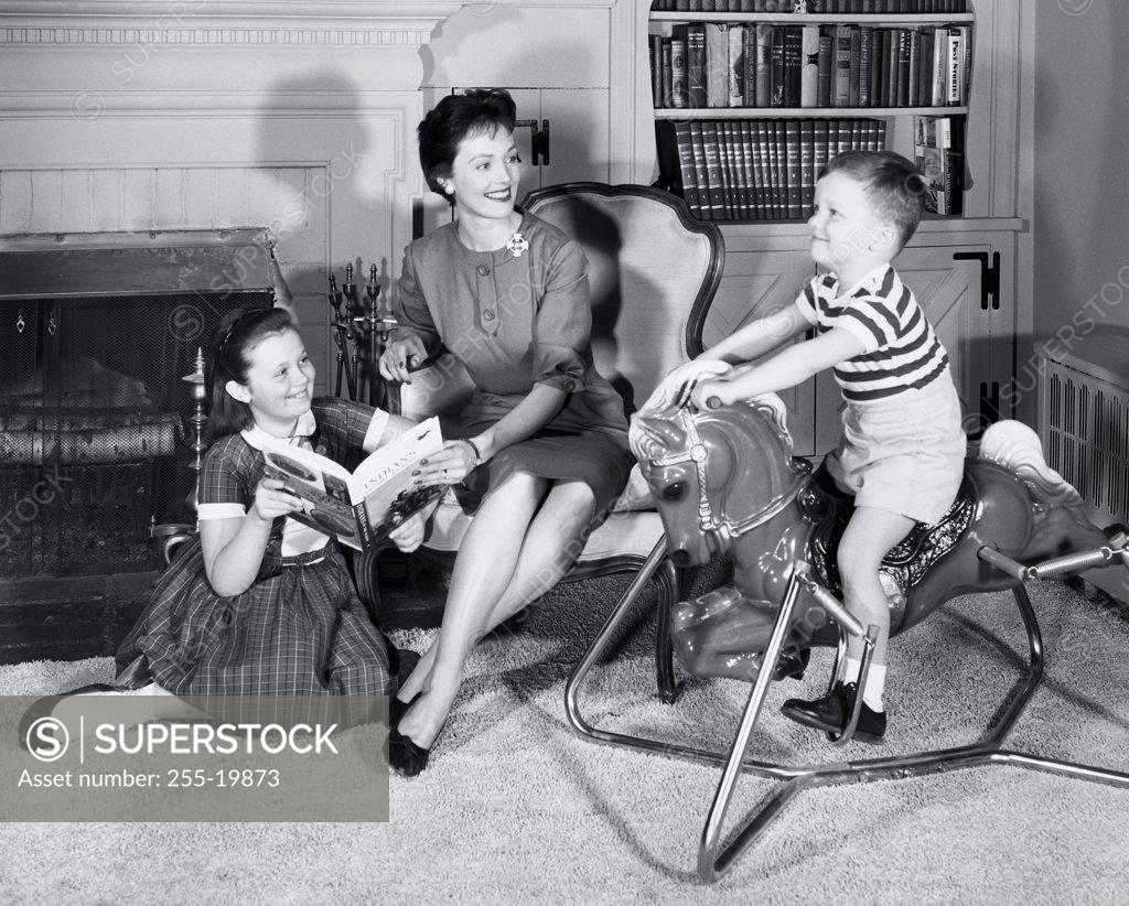 Stock Photo: 255-19873 Side profile of a boy sitting on a rocking horse with his mother and sister sitting beside him