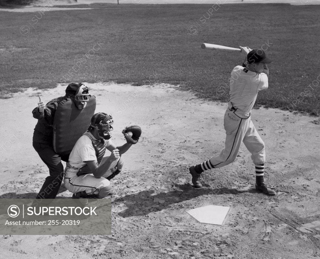 Stock Photo: 255-20319 Baseball player swinging a baseball bat with a baseball catcher and a baseball umpire crouching beside him