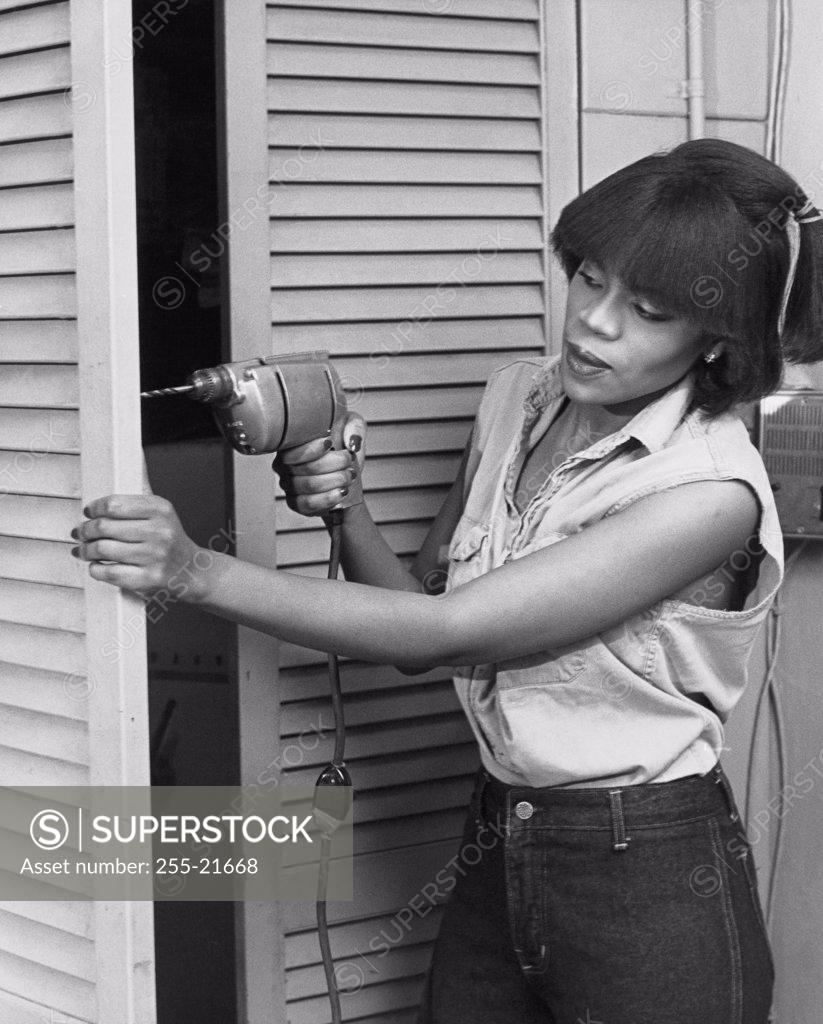 Stock Photo: 255-21668 Young woman drilling into a door