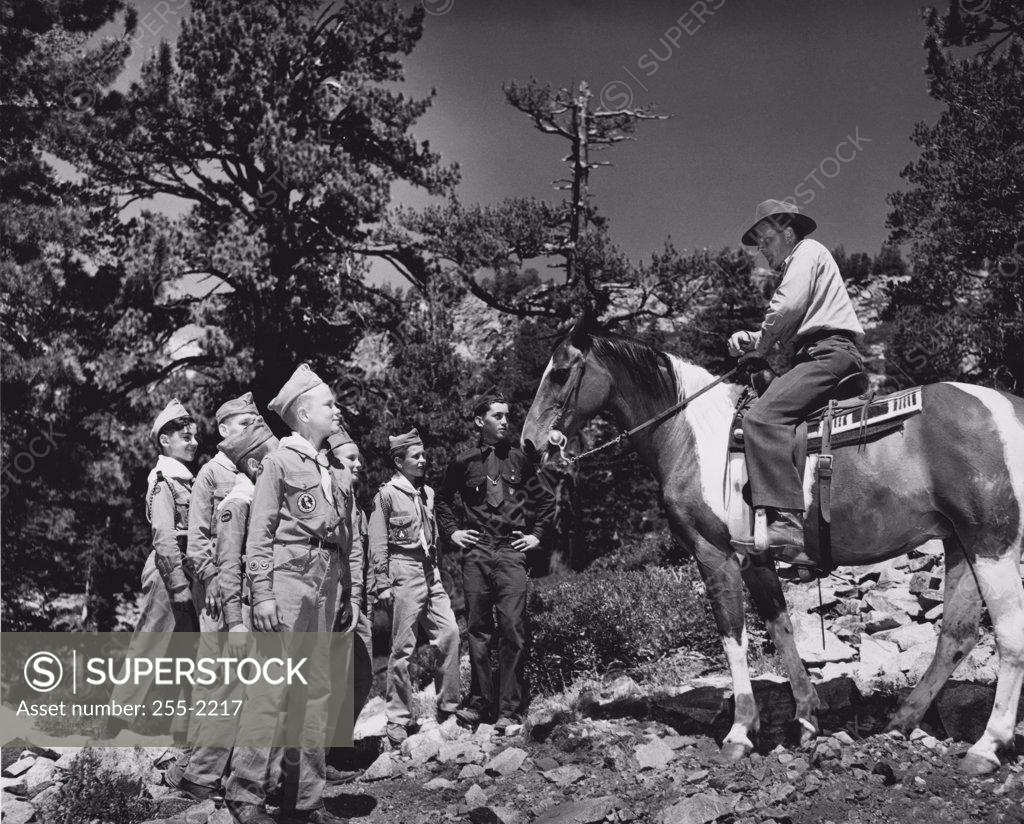Stock Photo: 255-2217 Side profile of a young man riding a horse in front of boy scouts at summer camp, Eldorado National Forest, California, USA