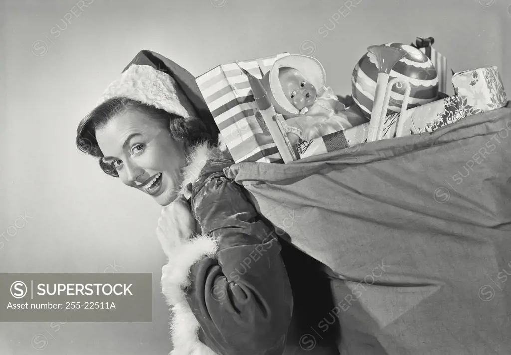 Brunette woman in Santa Claus hat carrying sack full of childrens toys