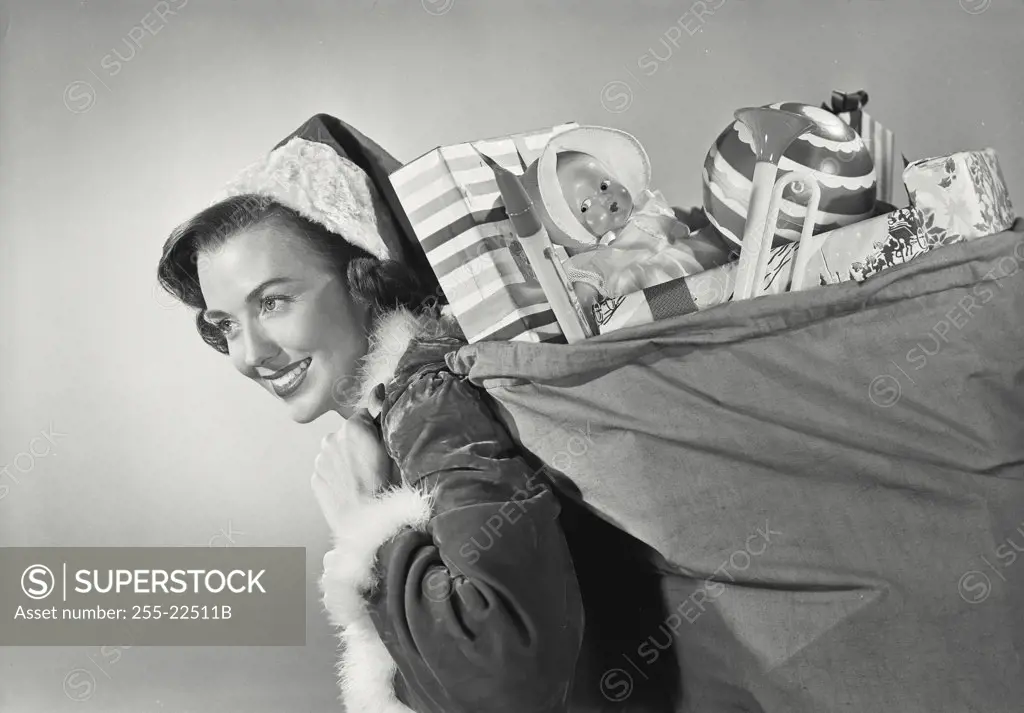 Close-up of a brunette woman in Santa Claus hat smiling carrying sack full of childrens toys