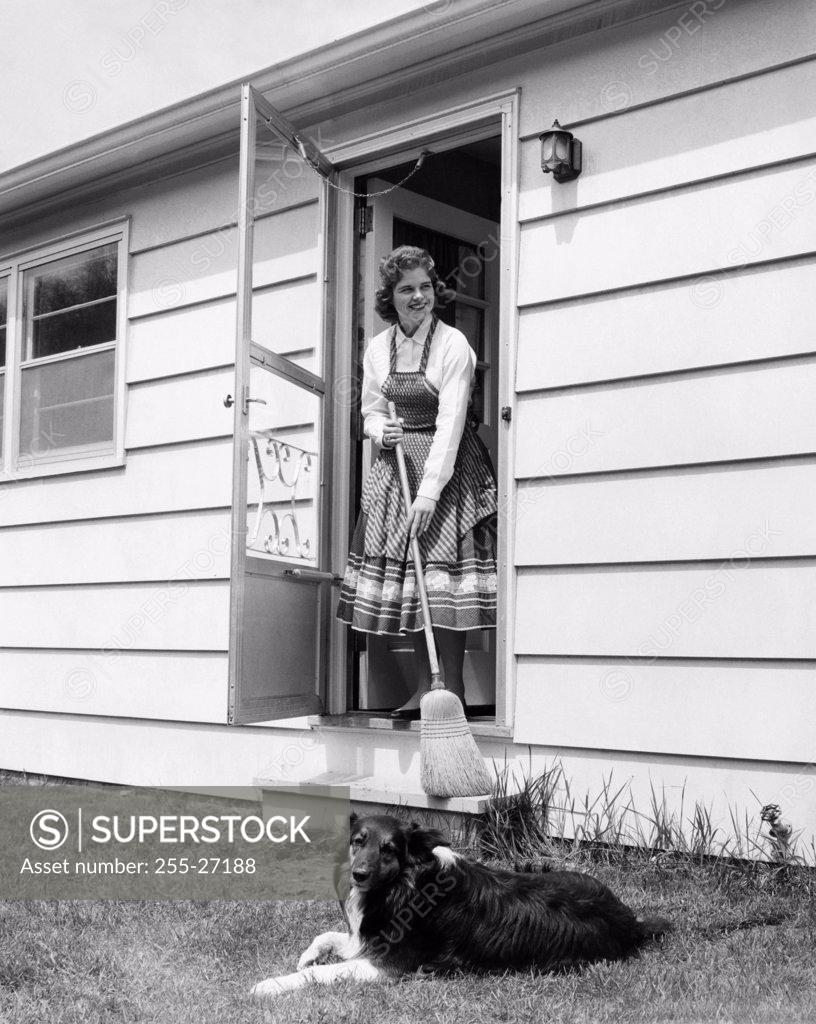 Stock Photo: 255-27188 Young woman standing at the doorstep holding a broom stick