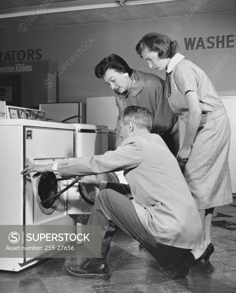 Stock Photo: 255-27656 Side profile of a salesman showing a washing machine to two female customers