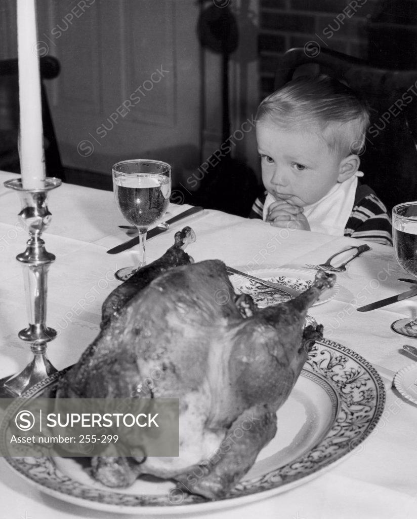 Stock Photo: 255-299 High angle view of a boy sitting at a dining table and looking at a roasted turkey on Thanksgiving day