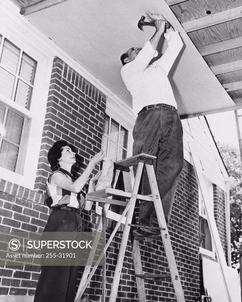 Stock Photo: 255-31901 Low angle view of a mid adult man fixing plywood on a porch with a mid adult woman helping him