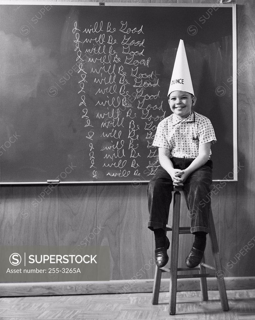 Stock Photo: 255-3265A Boy wearing a dunce cap sitting in front of a blackboard