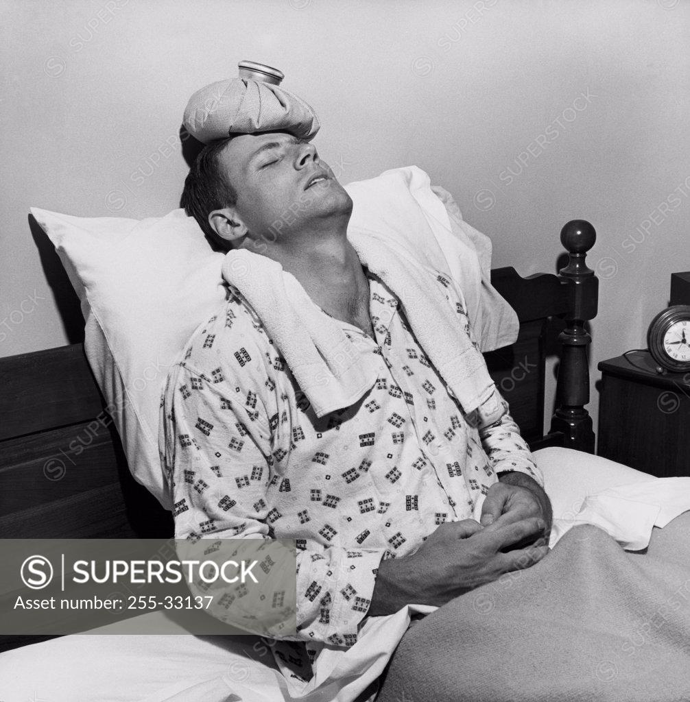 Stock Photo: 255-33137 Mature man reclining on the bed with an ice pack on his head