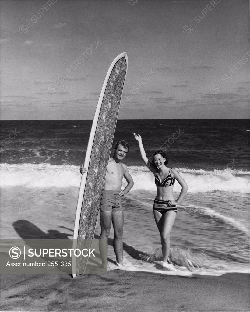 Stock Photo: 255-335 Young man holding surfboard on beach with young woman standing beside him