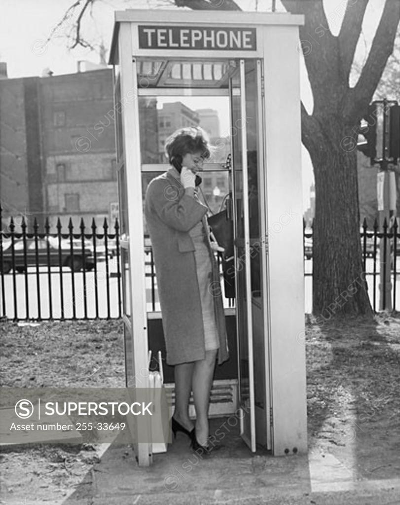 Stock Photo: 255-33649 Side profile of a young woman talking on the phone in a telephone booth