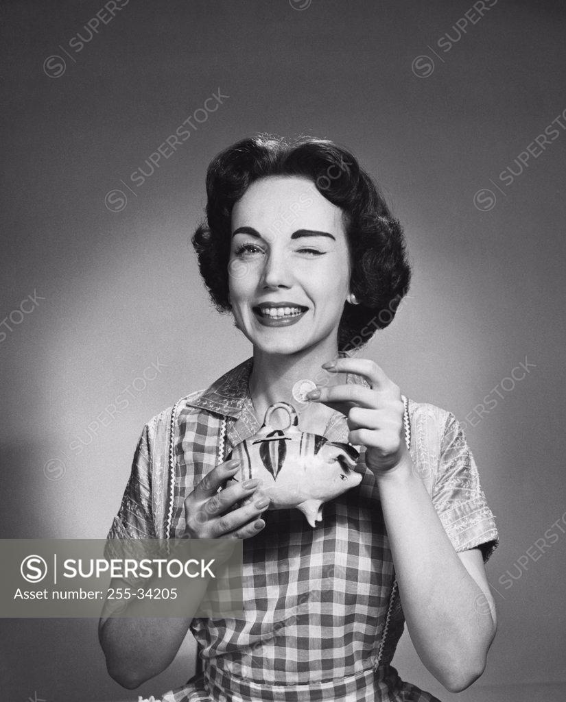 Stock Photo: 255-34205 Close-up of a young woman holding a piggy bank and winking