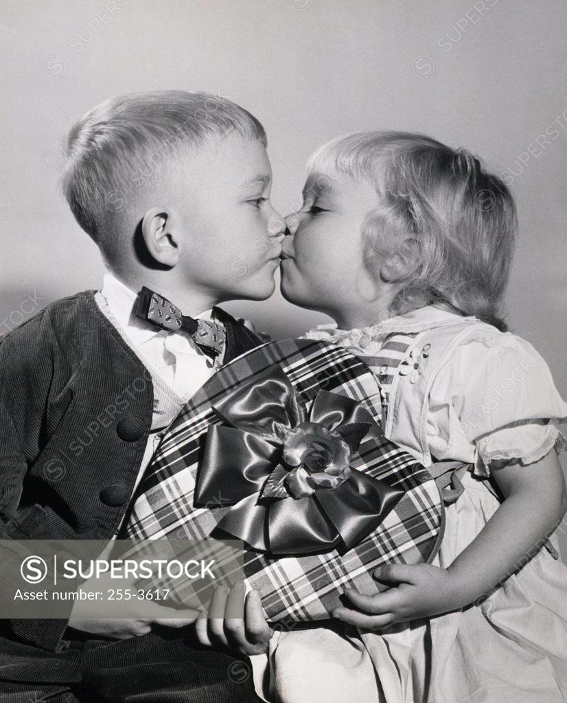 Stock Photo: 255-3617 Close-up of a boy and a girl holding a Valentine gift and kissing each other