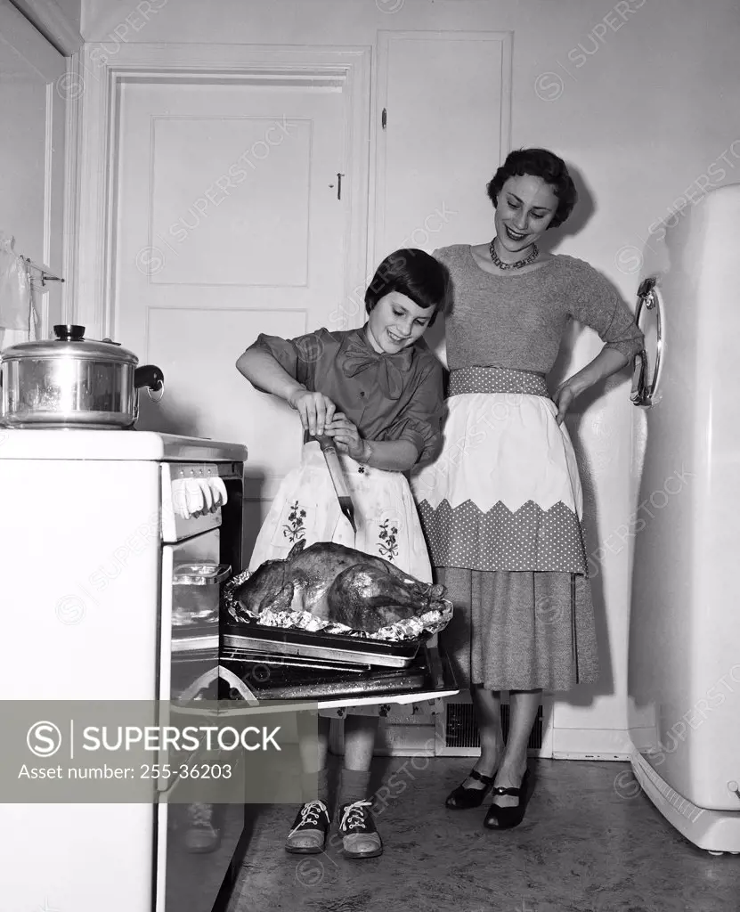 Mother looking at her daughter basting a turkey