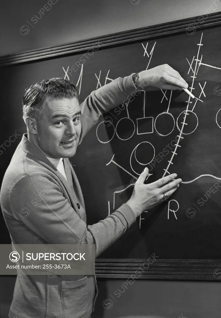 Picture of Football Coach in front of blackboard with plays.