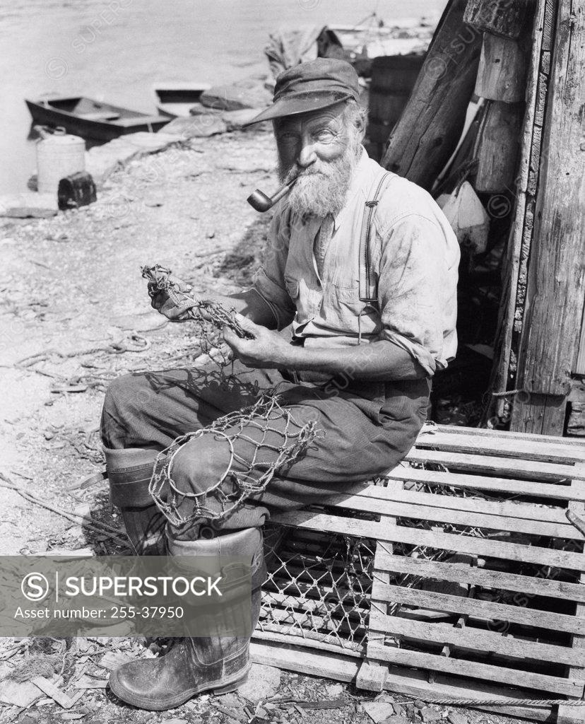 Stock Photo: 255-37950 Portrait of a fisherman sitting on a lobster trap and holding a fishing net