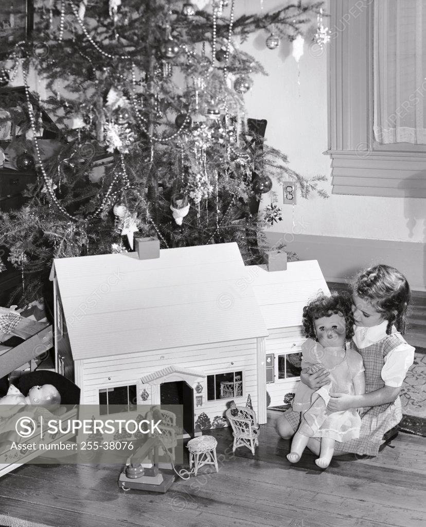Stock Photo: 255-38076 Girl sitting near a dollhouse and playing with a doll