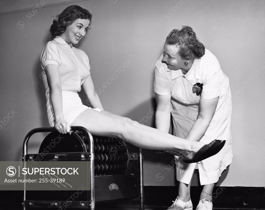 Stock Photo: 255-39189 Young woman exercising on an exercising machine with the help of a female instructor