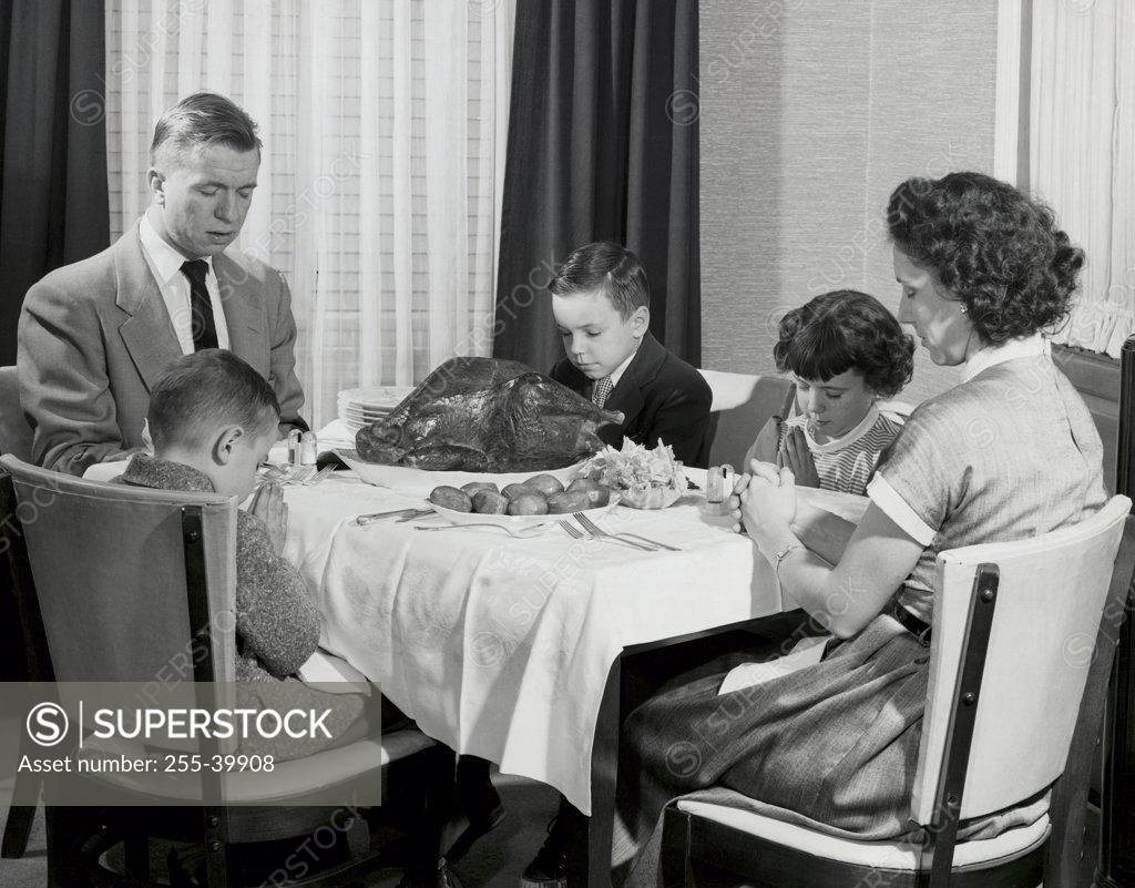 Stock Photo: 255-39908 Mature couple with their children praying at a dining table on Thanksgiving Day