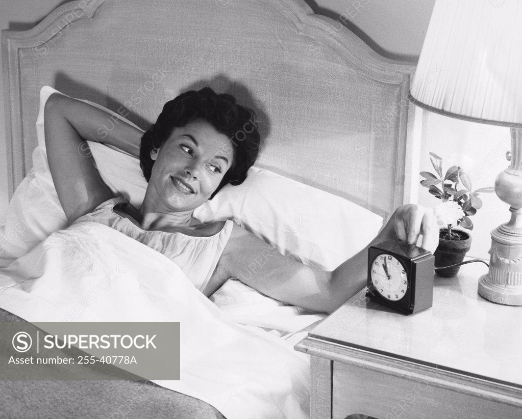 Stock Photo: 255-40778A High angle view of a young woman lying in the bed and turning on an alarm clock
