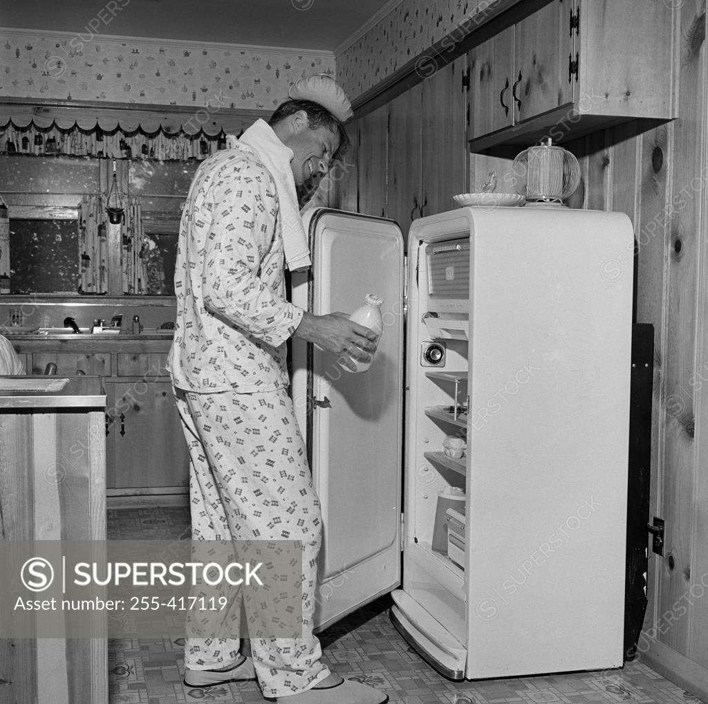 Stock Photo: 255-417119 Mid adult man wearing pajamas taking milk from fridge