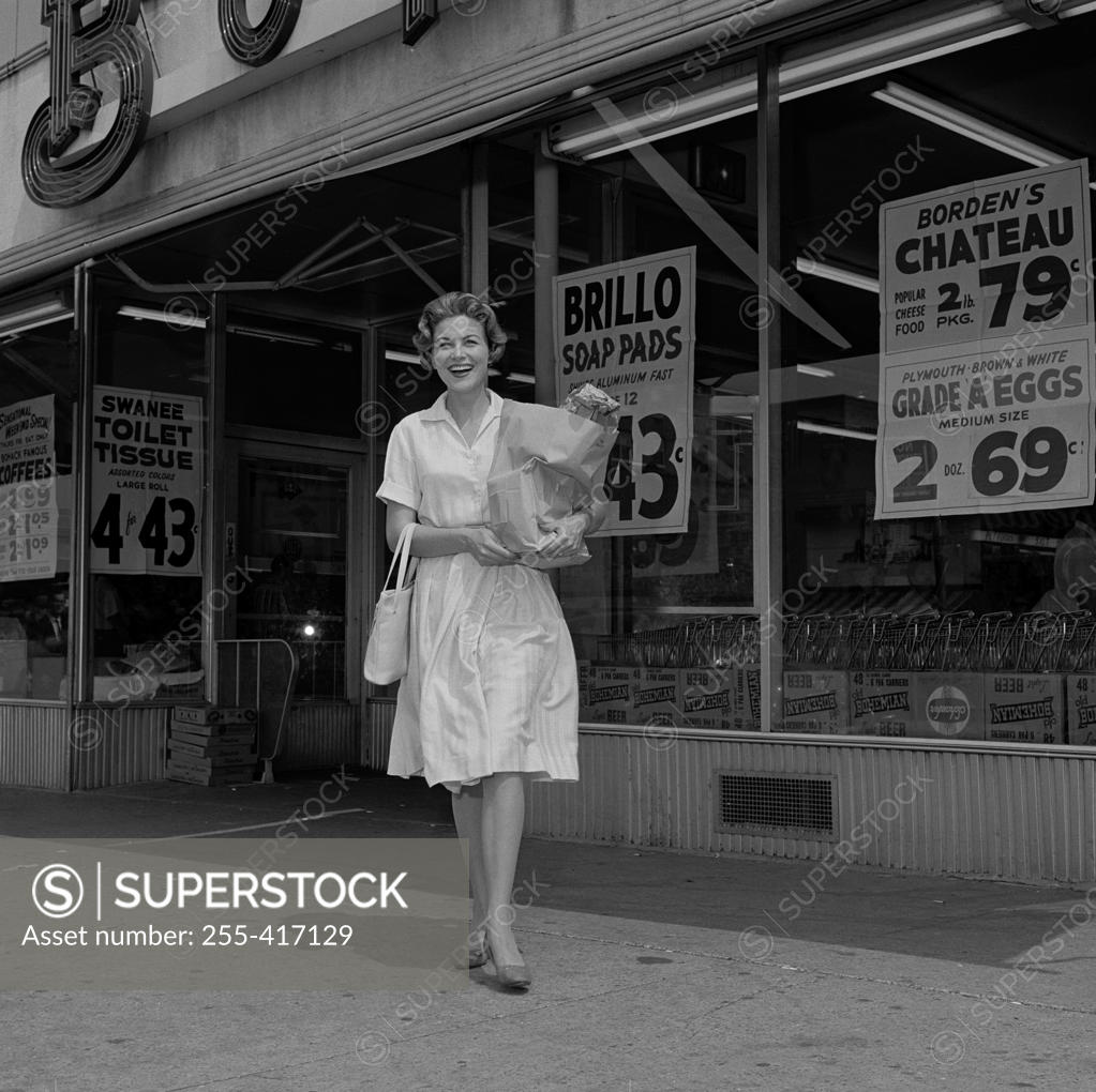 Stock Photo: 255-417129 Cheerful housewife outside supermarket, carrying shopping bag
