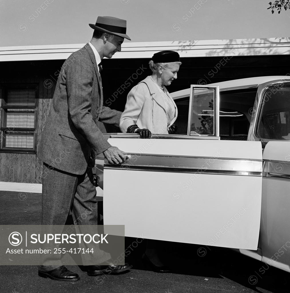 Stock Photo: 255-417144 Adult son holding car door open before mother