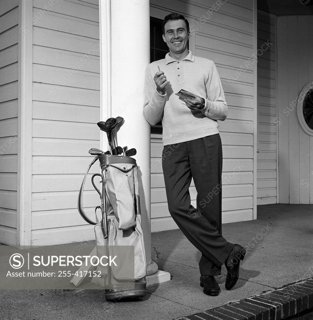 Stock Photo: 255-417152 Mid adult man leaning against column with golf trolley beside