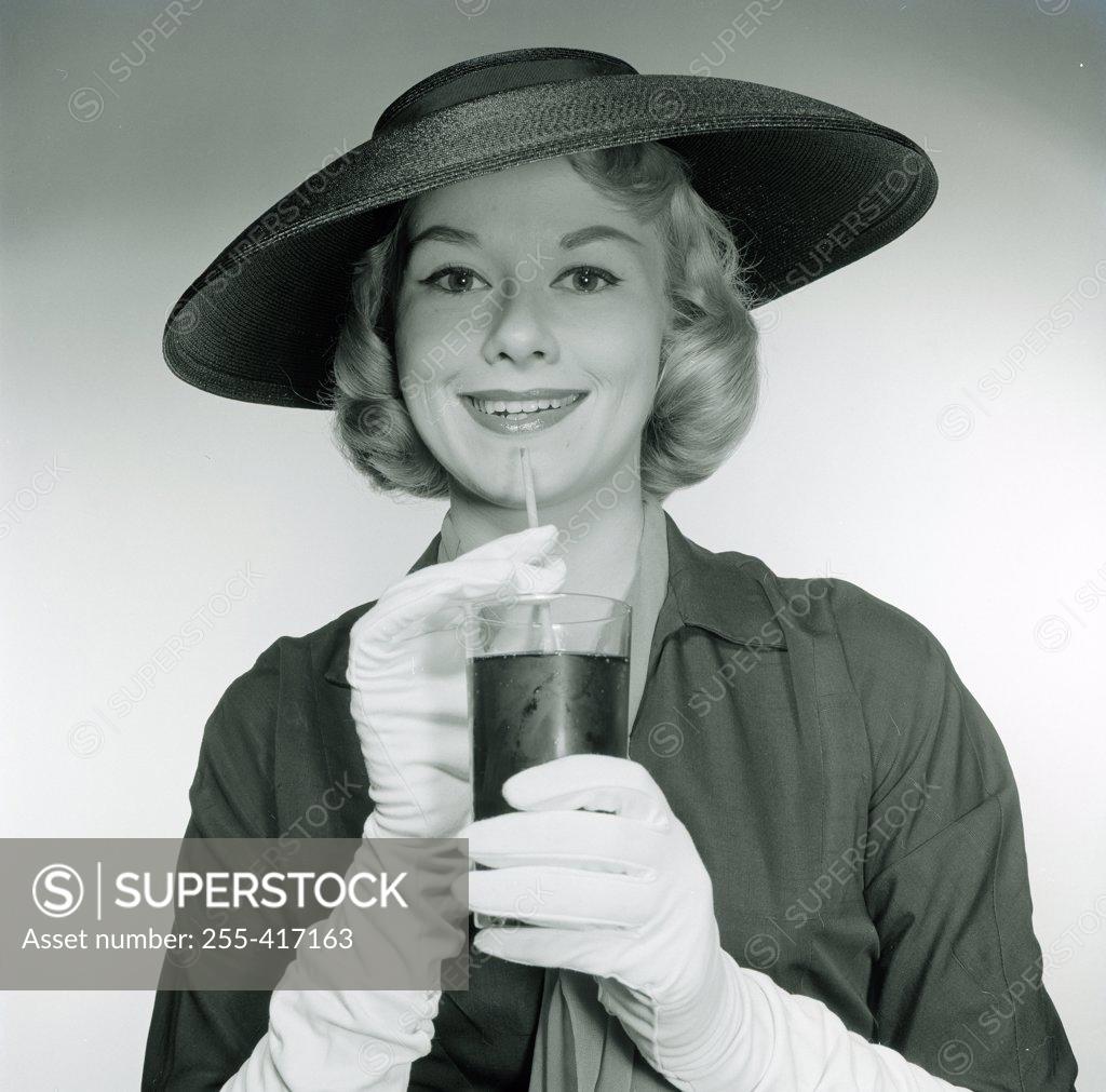 Stock Photo: 255-417163 Studio portrait of smiling young woman wearing hat and gloves, holding glass