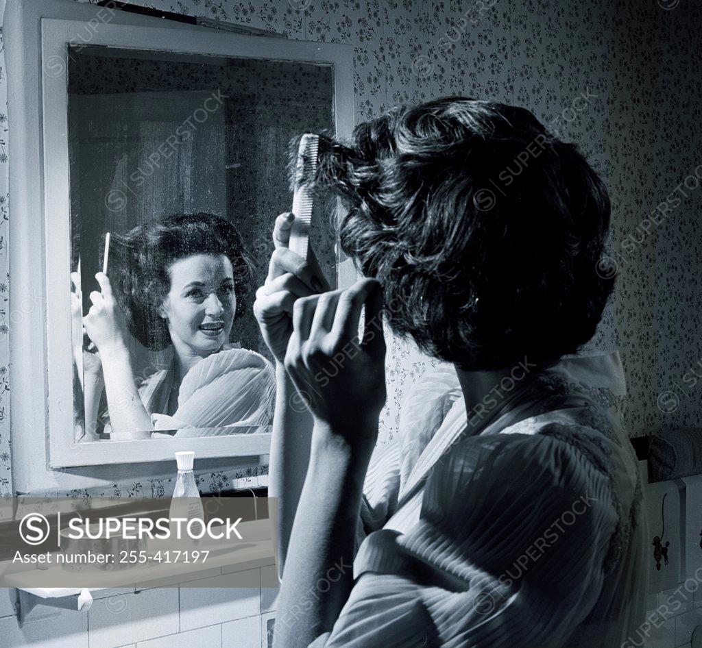 Stock Photo: 255-417197 Woman combing hair in front of mirror