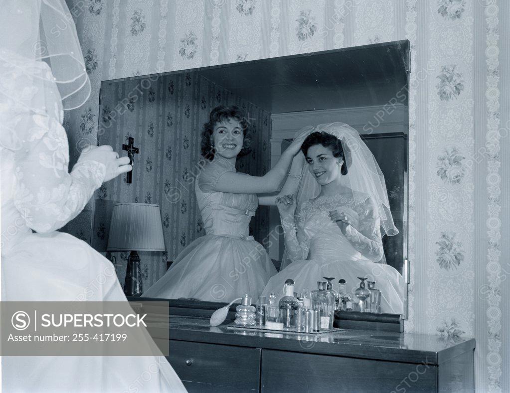 Stock Photo: 255-417199 Bridesmaid attaching veil to bride's hair in front of mirror