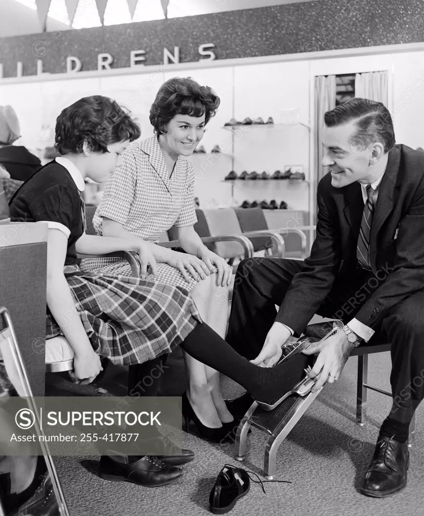 Shop assistant measuring girls foot in shoe shop