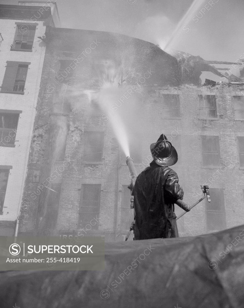 Stock Photo: 255-418419 Firefighter pouring water on burning building, low angle view