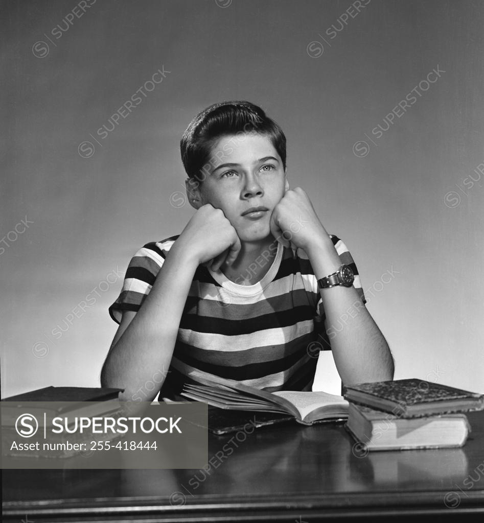 Stock Photo: 255-418444 teenage boy sitting wit books open and looking away