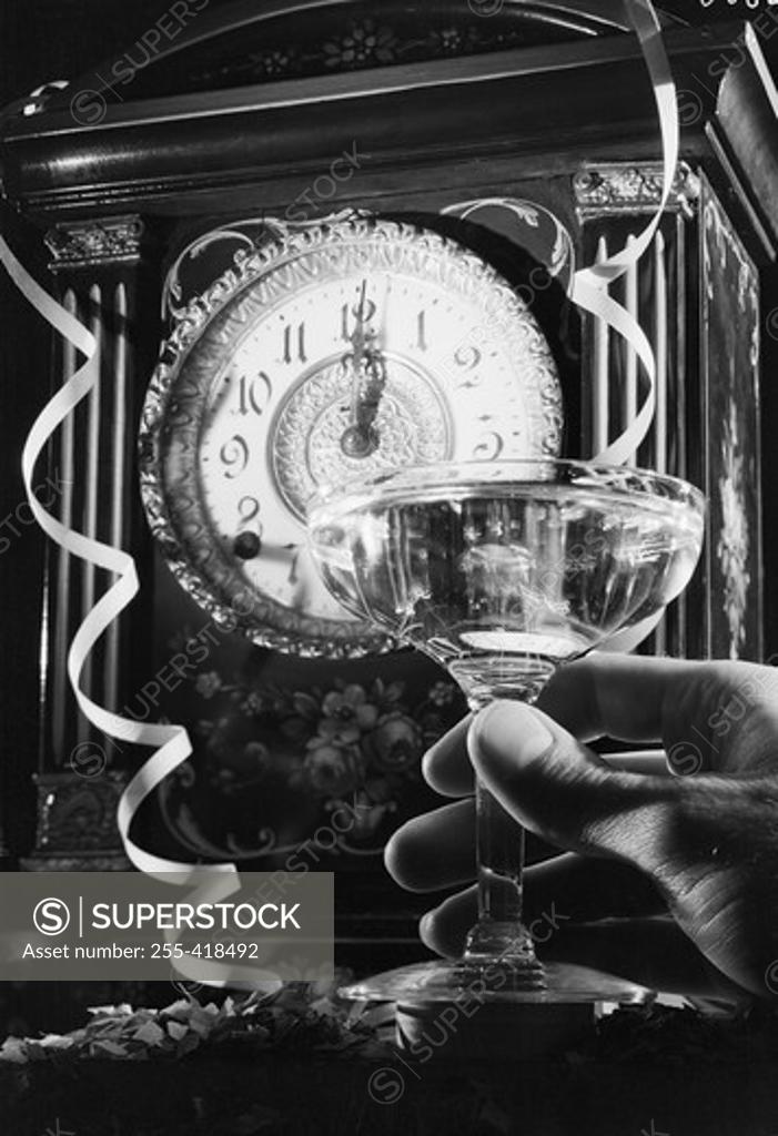 Stock Photo: 255-418492 Hand holding champagne flute with champagne, clock showing 12 o'clock in the background