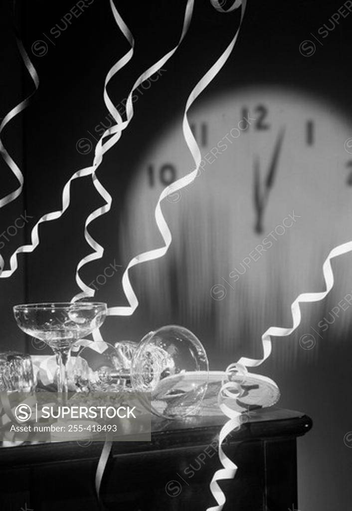 Stock Photo: 255-418493 Empty champagne flutes with streamers and clock face showing five past midnight